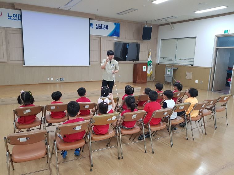 시각장애체험을 위해 흰지팡이 사용법에 대해 설명하는 담당자와 설명을 듣고 있는 아동들 모습